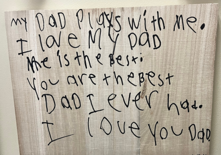 Wooden plaque made by Zachary Kovach's daughter. It hangs in his office and says "My dad plays with me. I love my dad. He is the best day I ever had. I love you dad."